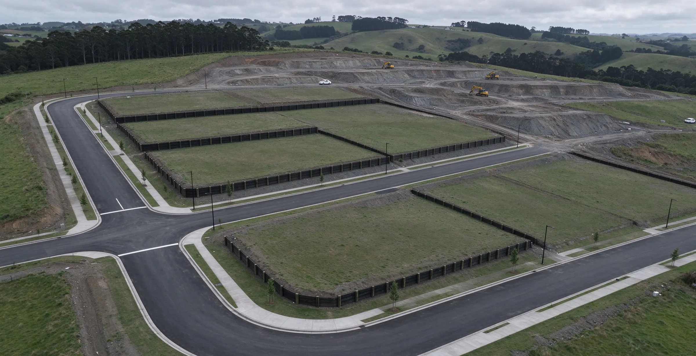 Aerial view of a new subdivision with sealed roads, retained grassed lots and earthworks under way beyond